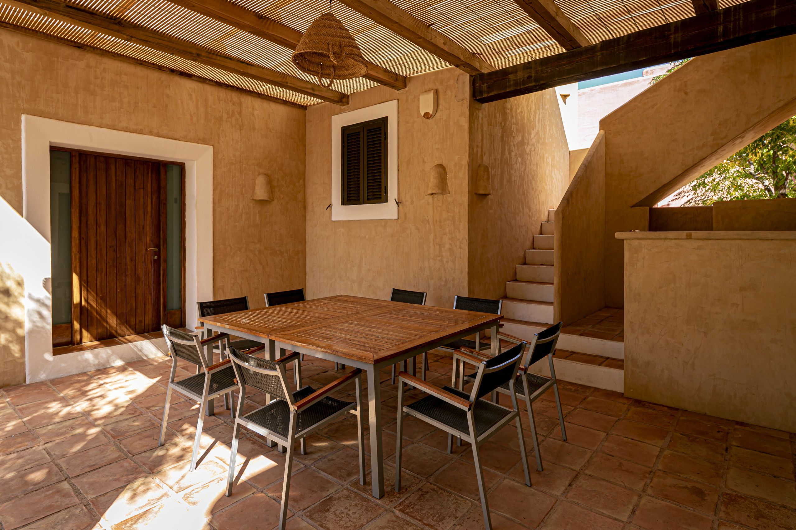 Un patio exterior con una mesa y sillas de madera, una puerta y una escalera que conduce a un nivel superior.