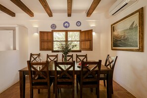 A dining room with a wooden table and chairs, a window with shutters, and a painting on the wall.