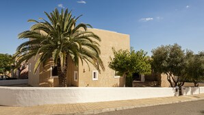 Un bâtiment à la façade plate, un palmier au premier plan et un ciel bleu dégagé.