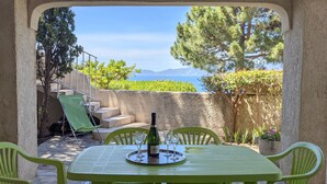 An outdoor patio with a table set for two, overlooking a scenic view of the sea and mountains. - Happyfew La petite Acacia (Coti-Chiavari)