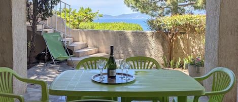 An outdoor patio with a table set for two, overlooking a scenic view of the sea and mountains.