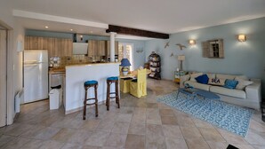 A spacious living area with a kitchen, a dining table, and a sofa with a 'SEA' pillow. - Happyfew La petite Acacia (Coti-Chiavari)