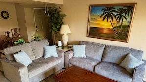 A living room with two grey sofas, a wooden coffee table, a painting of a sunset, and a potted plant.