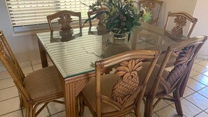 A dining table with a glass top surrounded by four chairs with woven seats and carved wooden backs.