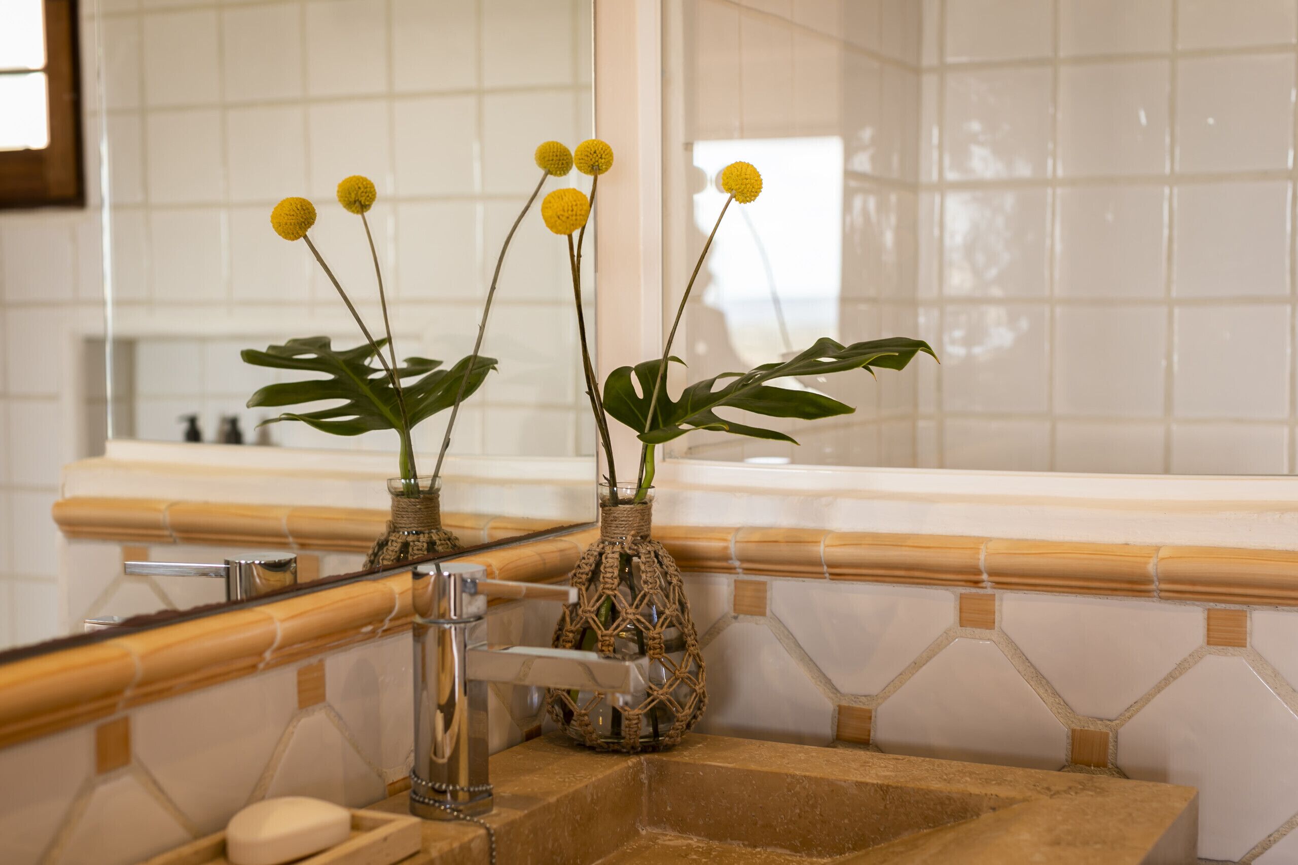 Un baño con lavamanos, espejo y dos jarrones decorativos con flores amarillas.