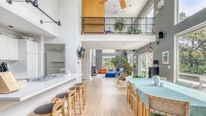 A modern kitchen with a central island, wooden chairs, and a dining area with a table and chairs. - Dunes Summer Retreat • Easy Walk to Private Ocean Beach (Amagansett)