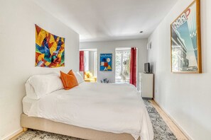 Een moderne slaapkamer met een groot bed, kleurrijke kunstwerken, een poster van Nord Express en een Bauhaus poster.
