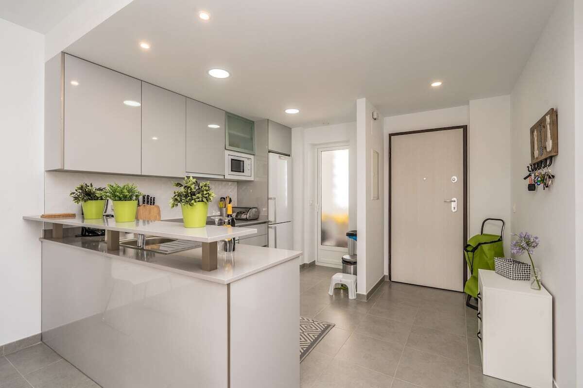 A modern kitchen with white cabinets, a central island, and potted plants.