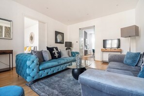 Un salon moderne avec un canapé bleu, un canapé gris, une table basse et un téléviseur.