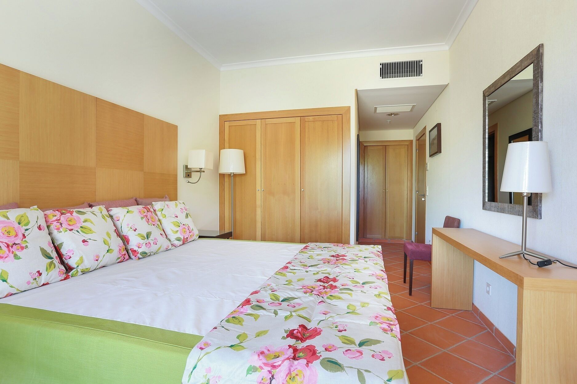 Une chambre d’hôtel comprenant un lit, un bureau, un miroir et une porte donnant sur une autre pièce.