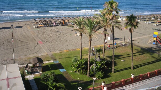A beach with palm trees, umbrellas, and a parking area. - Family studio 10 min walk from the beach (Benalmádena)