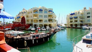 A marina with boats docked in front of a large, multi-story building with balconies. - Family studio 10 min walk from the beach (Benalmádena)