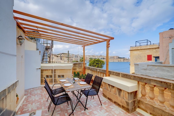 A terrace with a table set for two, overlooking a body of water and a cityscape. - Cosy Maltese Townhouse, Roof Terrace and Views (Senglea)