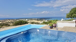 Ein Schwimmbecken mit Whirlpool, umgeben von Topfpflanzen, mit Blick auf eine Küstenlandschaft mit Gebäuden und blauem Himmel.