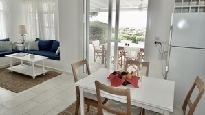 Ein modernes Wohnzimmer mit einem weißen Sofa, einem Couchtisch und einem Essbereich, dessen Tisch für zwei Personen gedeckt ist.