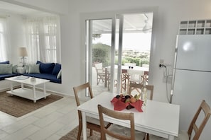 A modern living room with a white sofa, a coffee table, and a dining area with a table set for two. - Kamari Villa E: Greek Paradise with private pool & Jacuzzi (Naxos island)