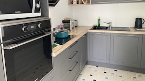Een moderne keuken met grijze kastjes, een zwarte oven, een magnetron, een broodrooster en een spoelbak.