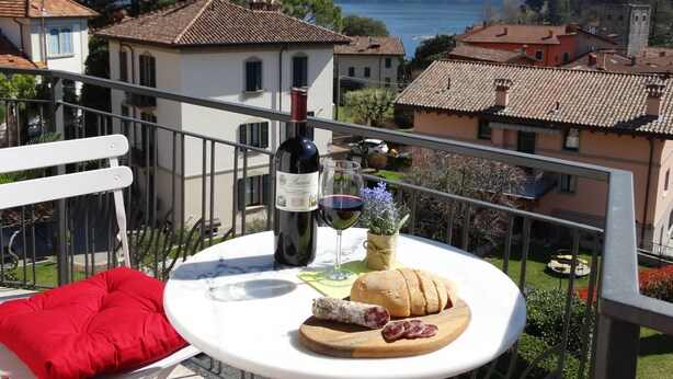 A balcony with a table set for a meal, a bottle of wine, and a view of a lake and mountains.