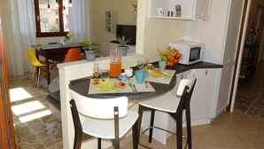 A compact kitchen with a dining area, featuring a small island with a fruit bowl, a microwave, and a sink.
