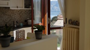 A kitchen with a view of the sea, a clock on the wall, and a potted plant on the counter.
