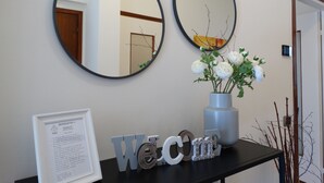 A reception area with two round mirrors, a welcome sign, a framed welcome letter, and a vase with white flowers.