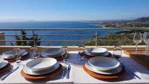 Mesa dispuesta para comer con vista al mar y al paisaje distante.