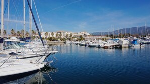 Un puerto deportivo con varios barcos amarrados, cielo despejado y edificios al fondo.