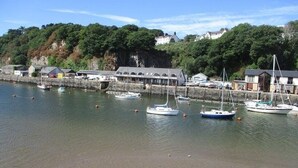 A harbor with boats docked, a building with a sloped roof, and a hillside with trees. - Sea View Holiday Cottage Porthmadog (Porthmadog)