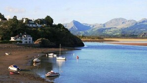 A coastal scene with boats on a calm water body, a house on a cliff, and mountains in the background. - Sea View Holiday Cottage Porthmadog (Porthmadog)