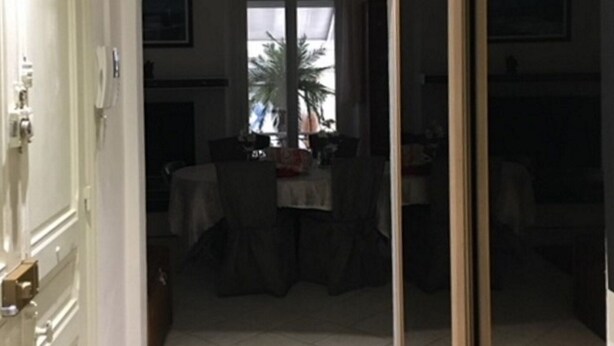 Um corredor com uma área de jantar ao fundo. Há duas imagens emolduradas na parede, uma porta à esquerda e uma porta de vidro à direita.