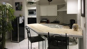 Uma cozinha moderna com armários brancos, uma ilha grande com banquetas, micro-ondas e um relógio na parede.