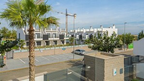 A modern building with a parking lot, a palm tree, and a construction crane in the background. - Apartamento Tulipanes (Pilar de la Horadada) (Pilar de la Horadada)