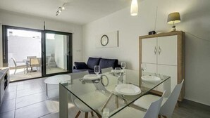 A modern dining area with a glass table and chairs, a white cabinet, and a sofa in the background. - Apartamento Tulipanes (Pilar de la Horadada) (Pilar de la Horadada)