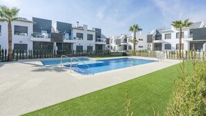 A modern residential complex with a swimming pool, surrounded by neatly trimmed grass and palm trees. - Apartamento Tulipanes (Pilar de la Horadada) (Pilar de la Horadada)