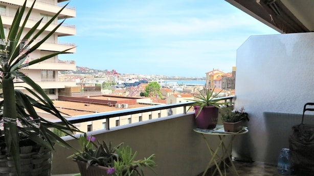 Een balkon met potplanten, uitzicht op een kustplaats en een heldere lucht.