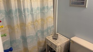 Un baño con cortina de ducha a rayas, un taburete de mimbre y un cuadro en la pared.