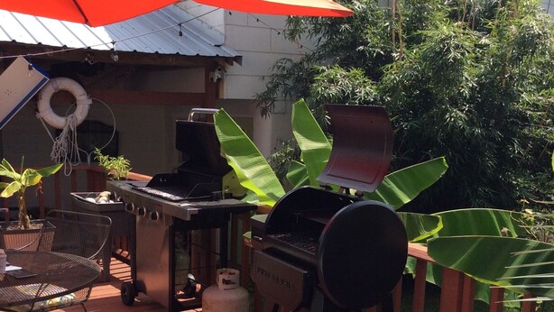 Una terraza de madera con una parrilla, una mesa de comedor y sillas.