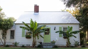 Una casa blanca con puerta y contraventanas verdes, techo de metal y el número 2717 en la fachada.