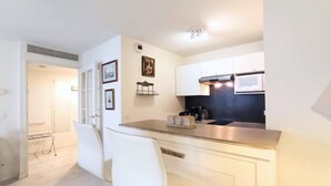Una cocina compacta con armarios blancos, encimera de acero inoxidable y horno empotrado. Tiene una pequeña isla con una silla y un marco de fotos en la pared.