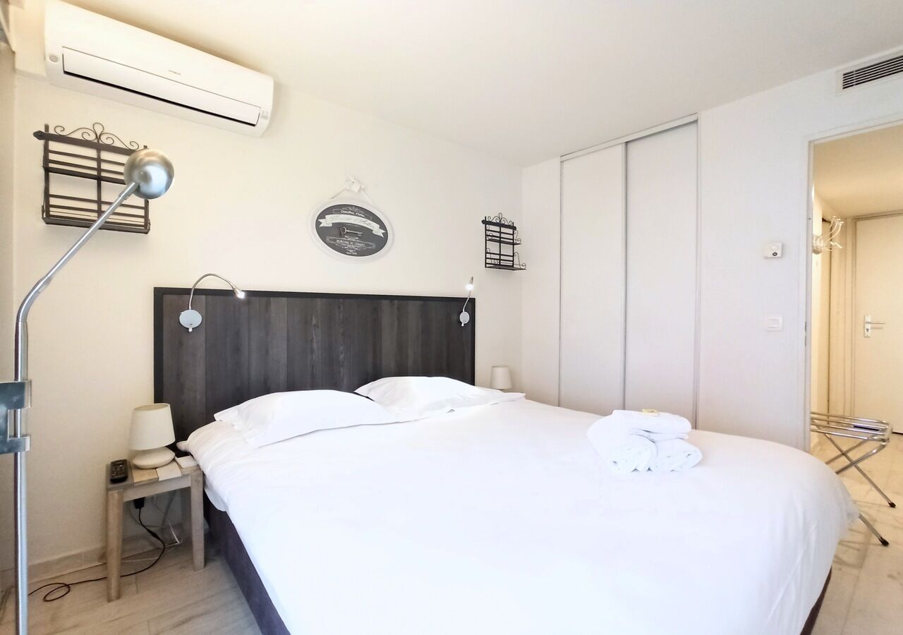 A neatly arranged hotel room with a bed, bedside table, lamp, and an air conditioning unit.