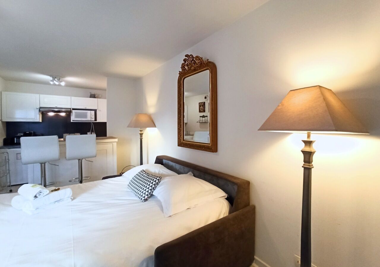 Een hotelkamer met een bed, nachtlampjes, een spiegel en een kitchenette op de achtergrond.