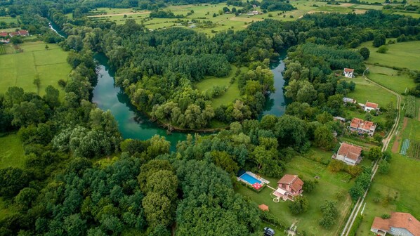 An aerial view of a rural area with a river, dense forests, and scattered houses.