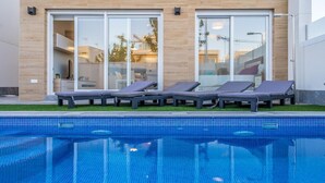 A modern pool area with a clear blue pool, lounge chairs, and a building with large glass doors. - Villa Sueño (San Pedro del Pinatar) (San Pedro del Pinatar)
