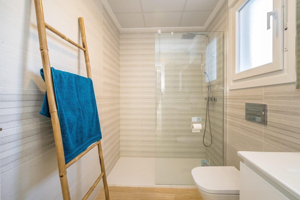 Une salle de bain avec une douche à parois de verre, des toilettes et une échelle en bois sur laquelle est posée une serviette bleue.