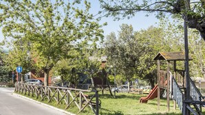 A playground with a slide and a small wooden structure, surrounded by trees and a fence. - S027 - Sirolo, new three-room apartment with terrace in the center (Sirolo)