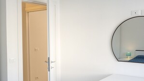 A room with a white door, a round mirror on the wall, and a small bedside table with a lamp. - S027 - Sirolo, new three-room apartment with terrace in the center (Sirolo)