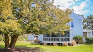 A two-story house with a porch, surrounded by a grassy yard and a large tree.