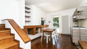 A modern kitchen with a dining area, wooden staircase, and a view of the outdoors.