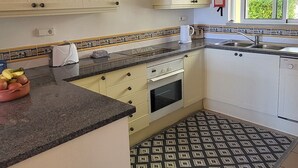 Une cuisine avec des meubles blancs, un plan de travail noir, un tapis à motifs et une fenêtre donnant sur un paysage verdoyant.