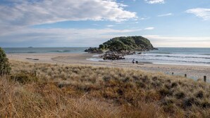 A beach with a grassy foreground, a rocky outcrop, and the sea. - Spacious Large Modern Apartment in Fantastic Location (Tauranga)